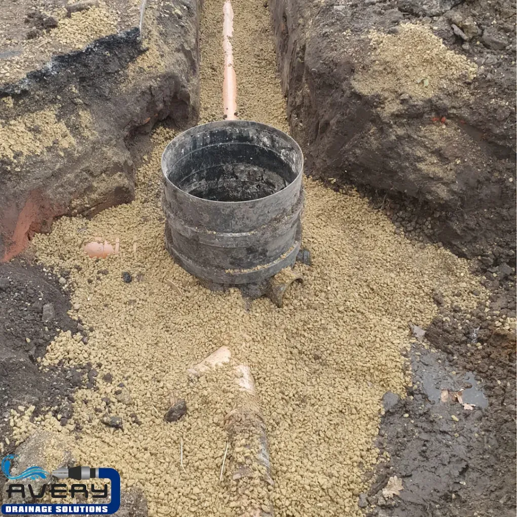 New drainage pipe and manhole base installation in a trench with gravel bedding.