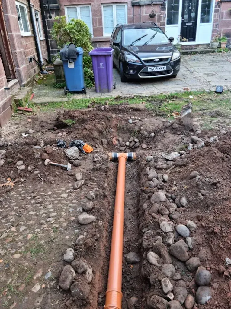 New orange drainage pipes being installed in a trench with soil and stones