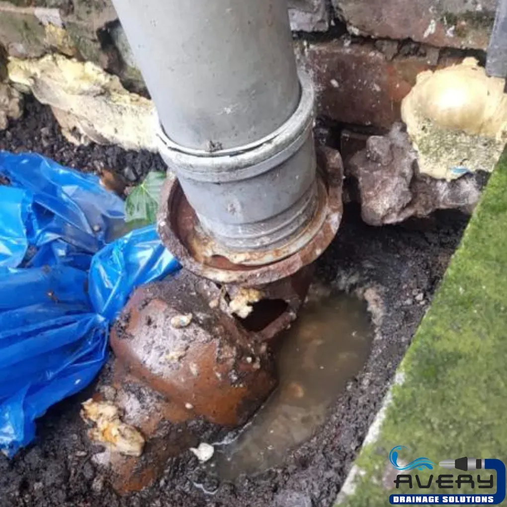 A broken drain pipe connection with standing water and debris.