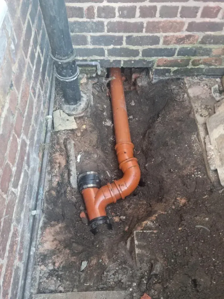 Newly installed drainage pipe during groundworks near a brick wall